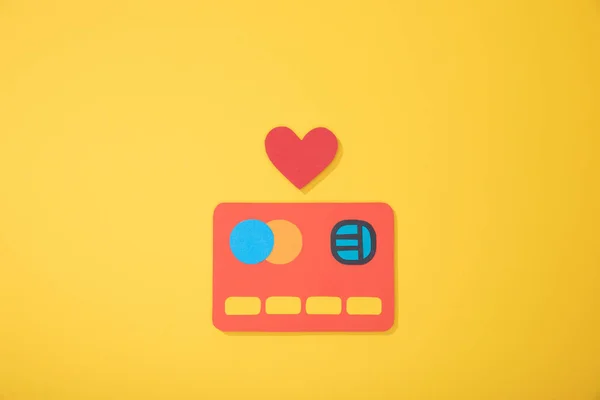 Vista superior do ícone de papel vermelho do cartão de crédito com coração de papel isolado no amarelo — Fotografia de Stock