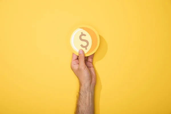 Cropped view of man holding paper icon of golden coin on yellow background — Stock Photo