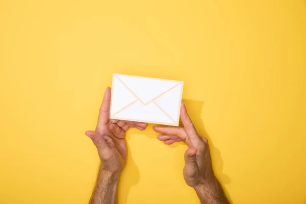 Обрезанный вид человека, держащего бумажную иконку конверта на желтом — стоковое фото