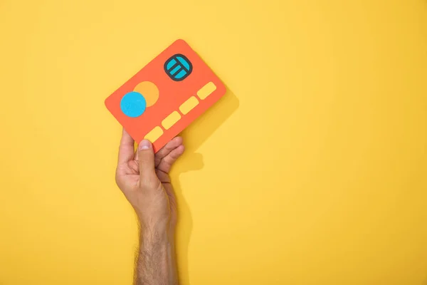 Vista cortada do homem segurando cartão de crédito papel vermelho no amarelo — Fotografia de Stock