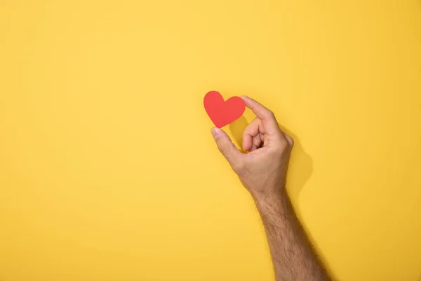 Обрезанный вид человека, держащего красное бумажное сердце на желтом — стоковое фото