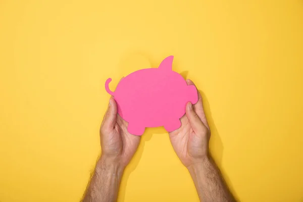 Cropped view of man holding pink paper piggy bank on yellow — Stock Photo