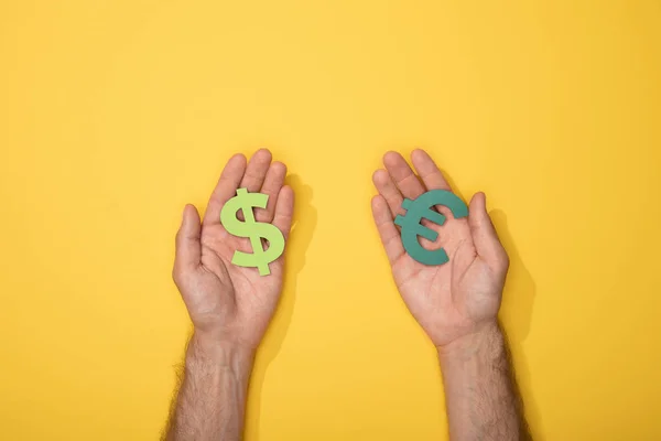 Vista cortada do homem segurando sinais de dólar e moeda do euro no amarelo — Fotografia de Stock