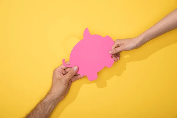 Cropped view of man and woman holding paper piggy bank on yellow — Stock Photo