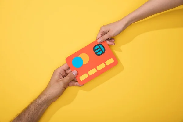 Cropped view of man and woman holding paper icon of credit card on yellow — Stock Photo