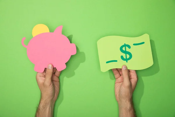 Cropped view of man holding paper icons of piggy bank and dollar banknote on green — Stock Photo