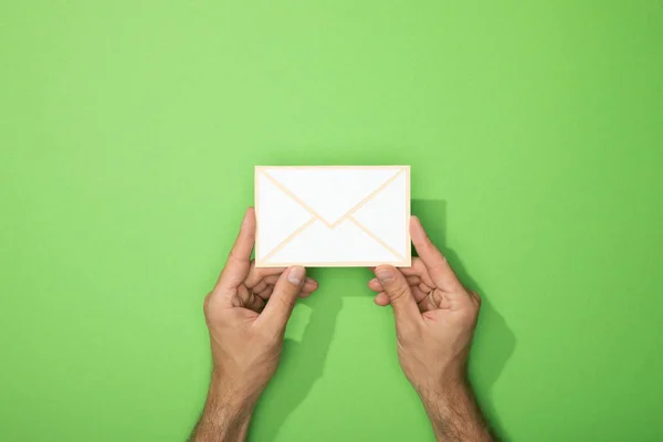 Vista recortada del hombre sosteniendo el icono de papel blanco de sobre en verde - foto de stock