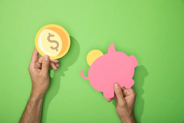 Vista cortada do homem segurando papel porquinho banco e moeda em verde — Fotografia de Stock