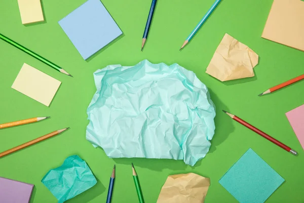 Вид сверху разбросанных кусочков скомканной бумаги рядом с карандашами на зеленом — стоковое фото