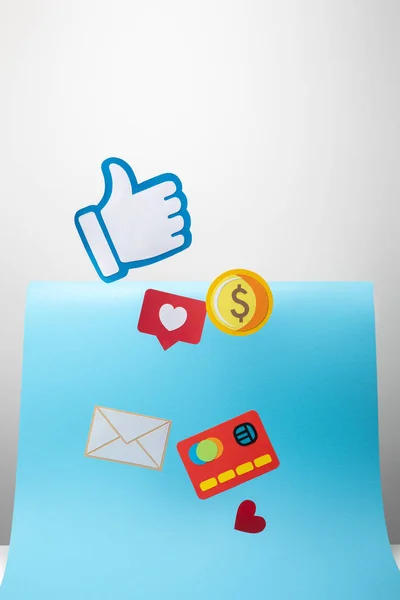 Paper icons with envelope, coin, credit card, hearts and thumb up on blue and grey background — Stock Photo