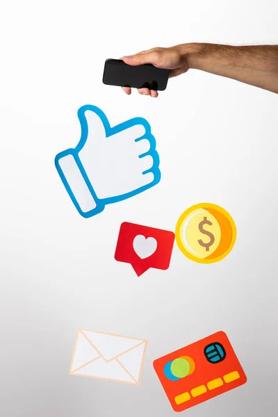 Cropped view of man holding smartphone above colorful paper icons on white — Stock Photo