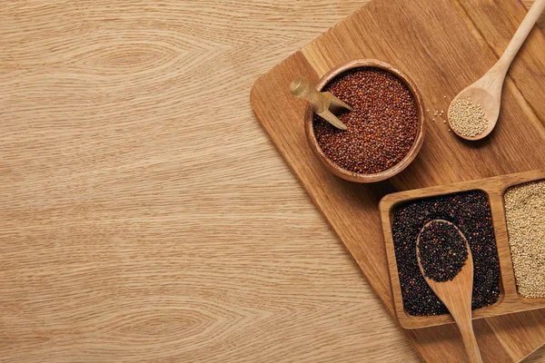 Top view of white, black and red quinoa in wooden bowls on chopping board — Stock Photo