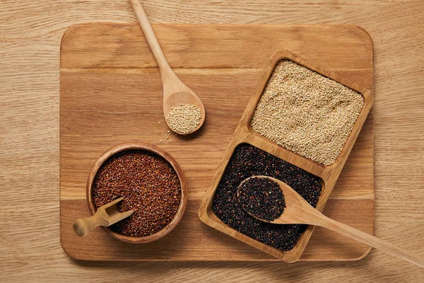 Vue du dessus du quinoa blanc, noir et rouge sur planche à découper en bois — Photo de stock