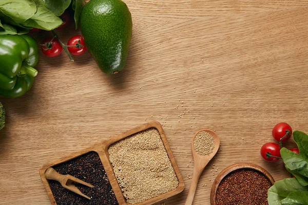 Ansicht von weißer, roter und schwarzer Quinoa in Schüsseln in der Nähe von reifem Gemüse und Löffel auf Holztisch — Stockfoto