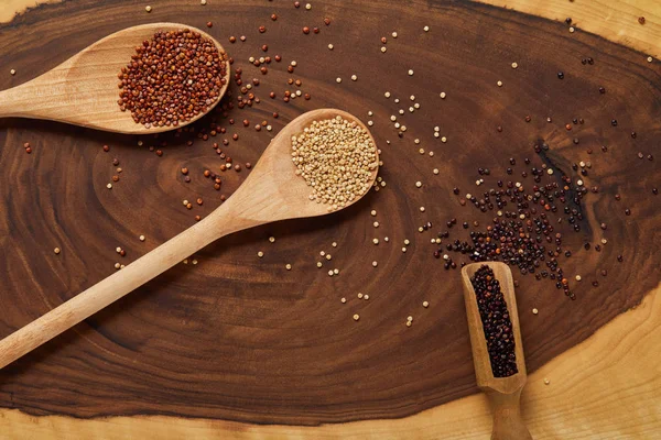 Top view of white, red and black quinoa in wooden spoon on beige and brown table — Stock Photo