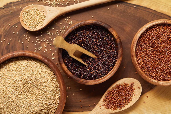 Close up view of white, black and red quinoa in wooden bowls with spatula and spoons — Stock Photo