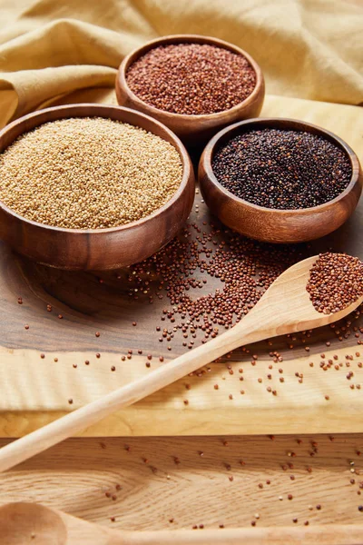 Quinoa bianca, nera e rossa in ciotole di legno e cucchiaio vicino al tovagliolo — Foto stock