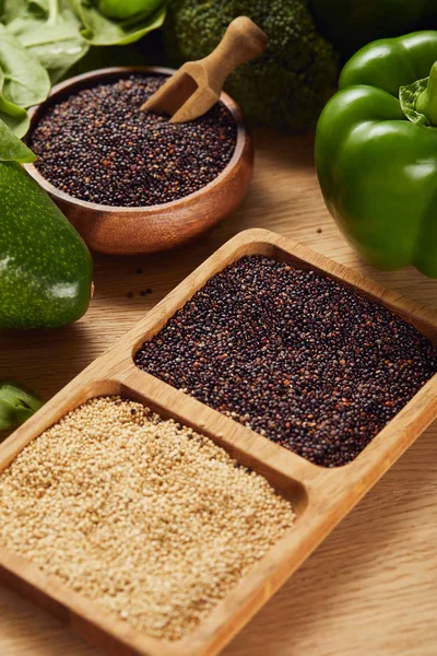 Schwarze und weiße Quinoa-Samen in hölzernen Schalen mit Spachtel in der Nähe von grünem Gemüse — Stockfoto