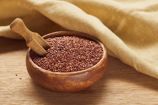 Red quinoa in wooden bowl with spatula near beige napkin — Stock Photo