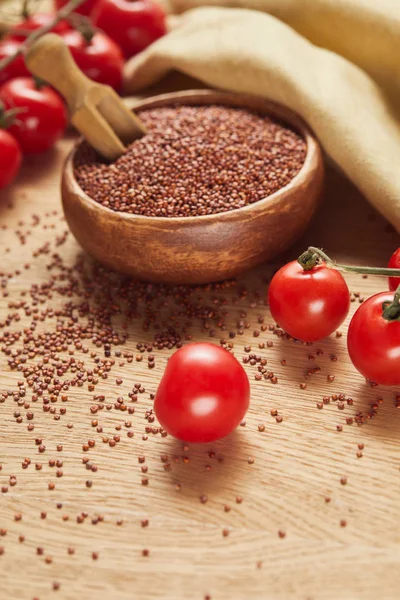 Selective focus of red quinoa in wooden bowl with spatula near beige napkin and scattered tomatoes — Stock Photo
