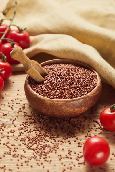 Quinoa rossa in ciotola di legno con spatola vicino tovagliolo beige e pomodori sparsi — Foto stock