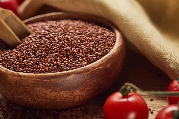 Close up view of red quinoa in wooden bowl with spatula near beige napkin and scattered tomatoes — Stock Photo