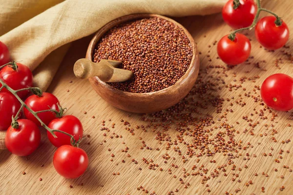 Quinua roja en cuenco de madera con espátula cerca de servilleta beige y tomates - foto de stock