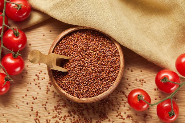 Top view of red quinoa in wooden bowl with spatula near beige napkin and tomatoes — Stock Photo