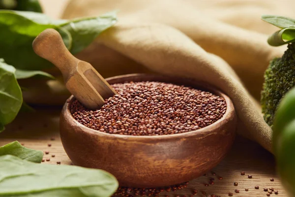Nahaufnahme von rotem Quinoa in Holzschale mit Spachtel in der Nähe von beiger Serviette und grünem Gemüse — Stockfoto