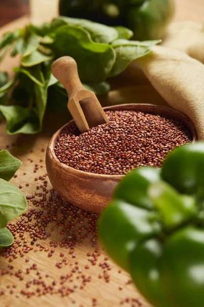 Selective focus of green bell pepper and red quinoa in wooden bowl with spatula near beige napkin — Stock Photo