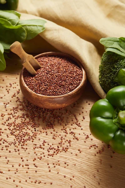 Red quinoa in wooden bowl with spatula near beige napkin and green ripe vegetables — Stock Photo