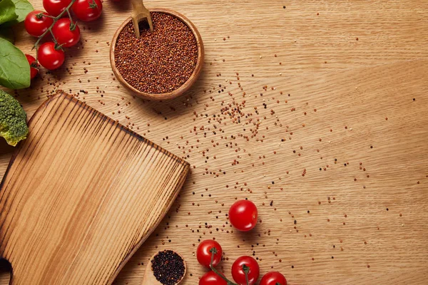 Top view of red quinoa seeds in wooden bowl near chopping board and red tomatoes — Stock Photo