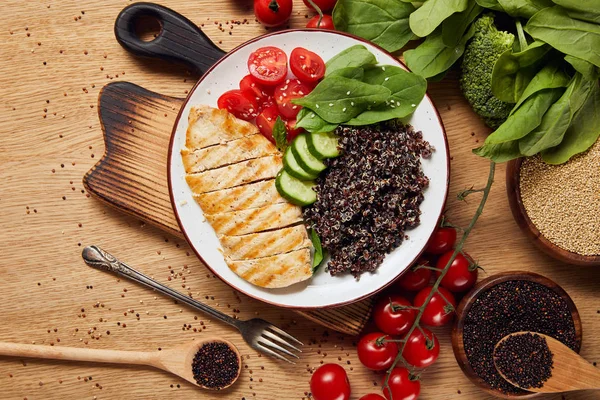 Vue du dessus du quinoa cuit avec poitrine de poulet grillée et légumes sur plaque blanche sur planche à découper en bois — Photo de stock