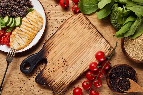 Vista superior de la quinua cocida con pechuga de pollo a la parrilla y verduras en plato blanco sobre mesa de madera - foto de stock