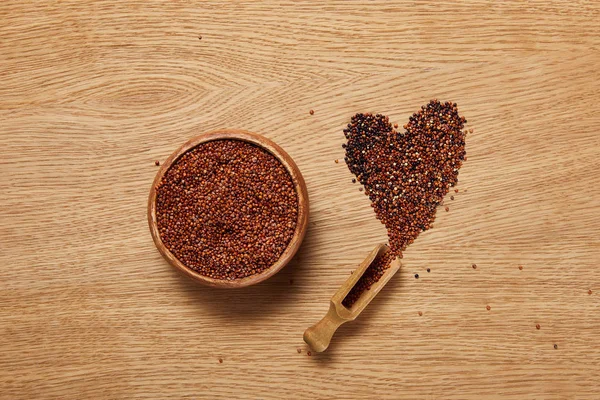 Vue du dessus des graines de quinoa rouge dans un bol en bois près du signe cardiaque et de la spatule — Photo de stock