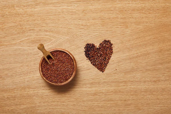 Vue du dessus des graines de quinoa rouge dans un bol en bois avec spatule près du signe cardiaque — Photo de stock