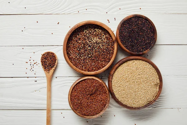 Vista superior da quinoa branca, preta e vermelha em tigelas de madeira perto da colher na mesa branca — Fotografia de Stock