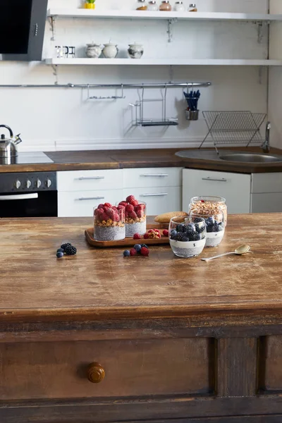 Gustoso yogurt con semi di chia e bacche in bicchieri su vassoio di legno in cucina — Foto stock