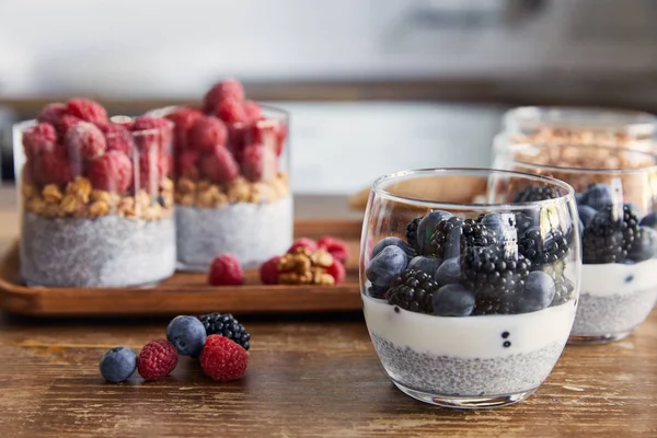 Selektiver Fokus von Joghurt mit Chiasamen, Himbeeren, Blaubeeren und Brombeeren in Gläsern in der Küche — Stockfoto