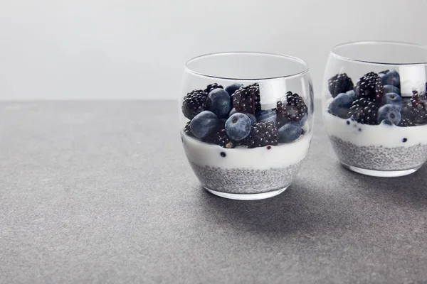 Delicioso iogurte com sementes de chia e bagas em óculos isolados em cinza — Fotografia de Stock