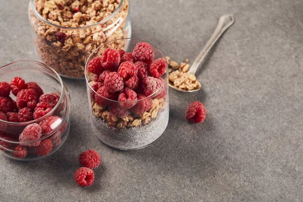 Yogurt con semi di chia, fiocchi d'avena e lamponi vicino a cucchiaino con avena sulla superficie di marmo — Foto stock