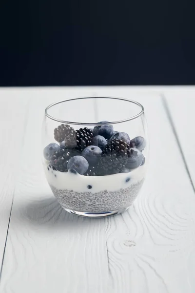 Glas mit Blaubeeren, Brombeeren und Joghurt mit Chiasamen auf weißem Holztisch isoliert auf schwarzem — Stockfoto