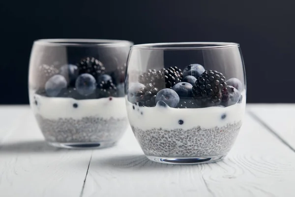 Focus selettivo di yogurt con semi di chia, mirtilli, more su legno bianco isolato su nero — Foto stock