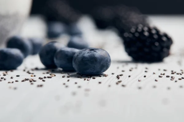 Nahaufnahme von Blaubeeren, Brombeeren und verstreuten Chiasamen auf weißem Holztisch — Stockfoto