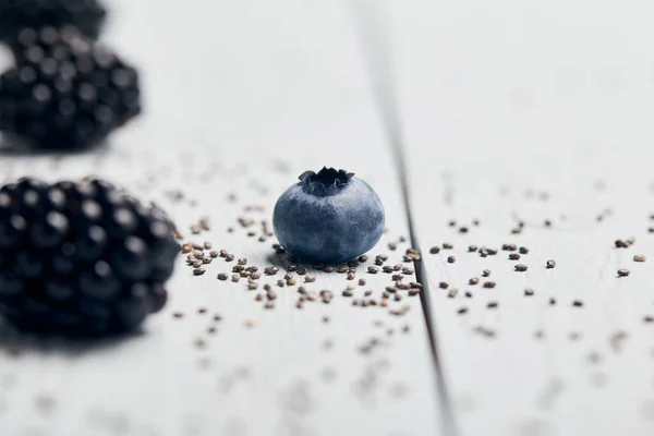 Vue rapprochée des myrtilles, mûres et graines de chia éparpillées sur table en bois blanc — Photo de stock