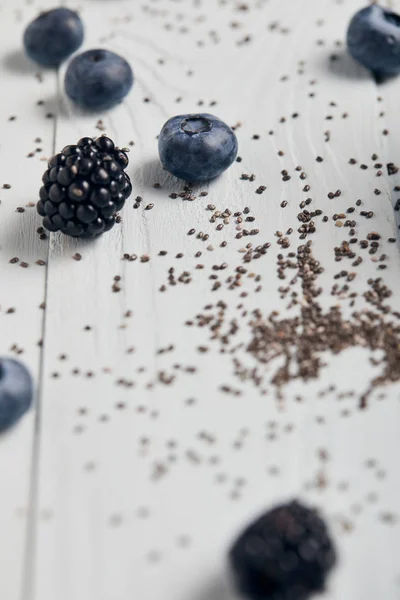 Vue rapprochée des myrtilles, mûres et graines de chia éparpillées sur une table en bois blanc — Photo de stock