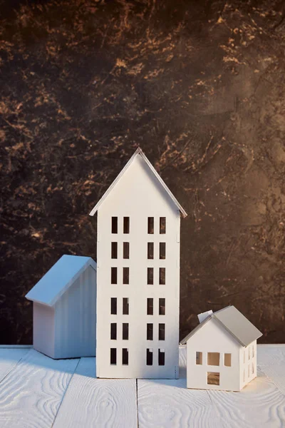 Casas modelos en mesa de madera blanca cerca de la pared de textura marrón, concepto de bienes raíces - foto de stock