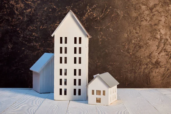 Maisons modèles sur table en bois blanc près du mur texturé brun, concept immobilier — Photo de stock