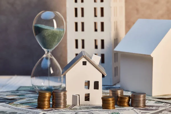 Houses models and hourglass on cash and coins, real estate concept — Stock Photo