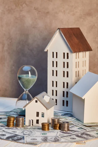 Houses models and hourglass on cash and coins, real estate concept — Stock Photo